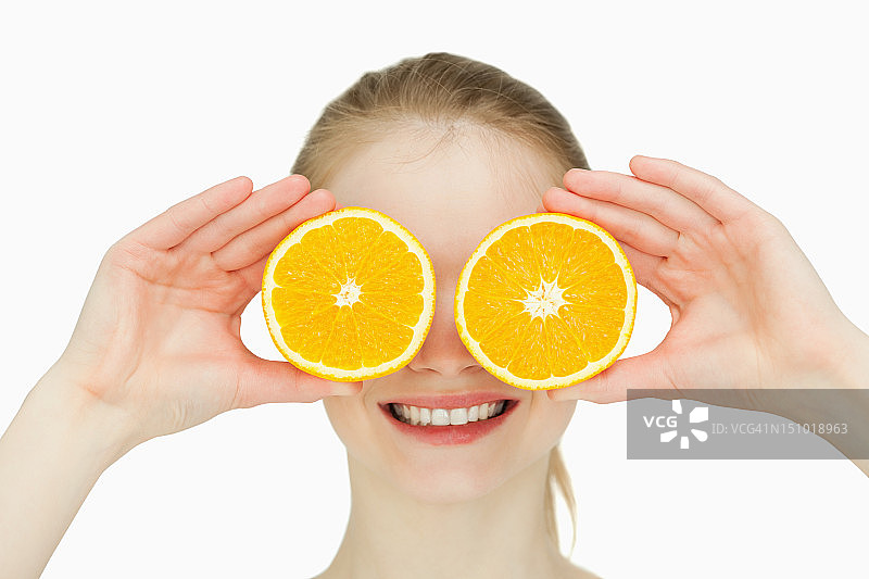 一个微笑的女人把橙子放在眼睛上的特写图片素材