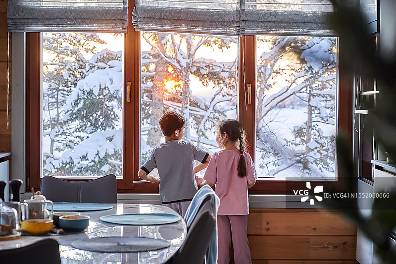 男孩和女孩站在窗前，看着冬天的风景。图片素材