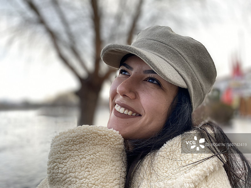 土耳其，站在湖边，戴着帽子微笑的女人看向别处的特写图片素材