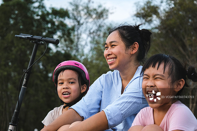 泰国，母亲和孩子在公园里骑完摩托车后坐下来休息图片素材