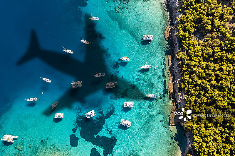 飞机飞过岛的海岸，游艇在碧绿的海水中。希腊图片素材