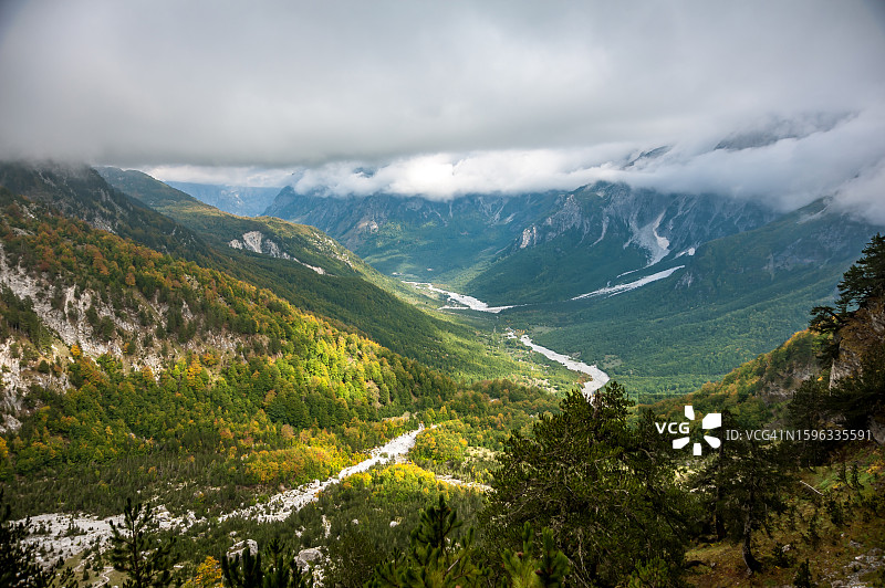 阳光透过低矮的云层照射在山谷、河流、陡峭的山脉和森林上图片素材