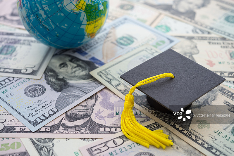 毕业帽或帽子印在美元钞票和全球世界背景上。图片素材