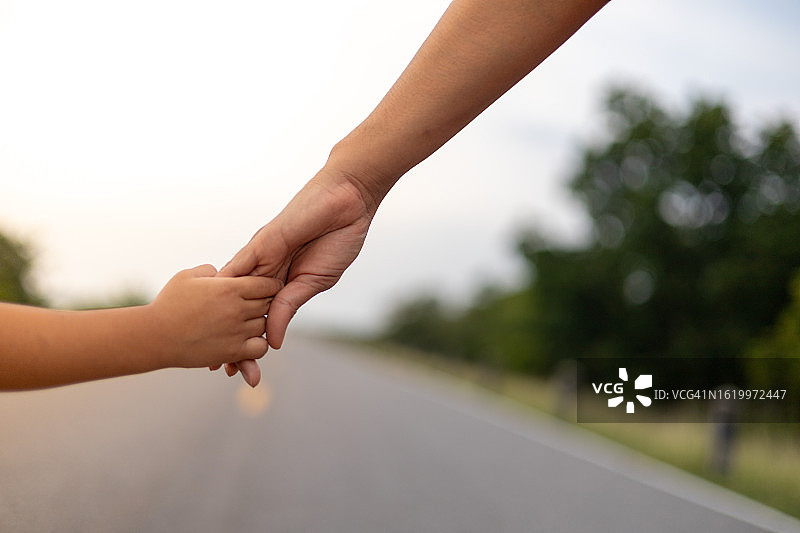 母亲和孩子的手牵着手走在路上。在夕阳下图片素材