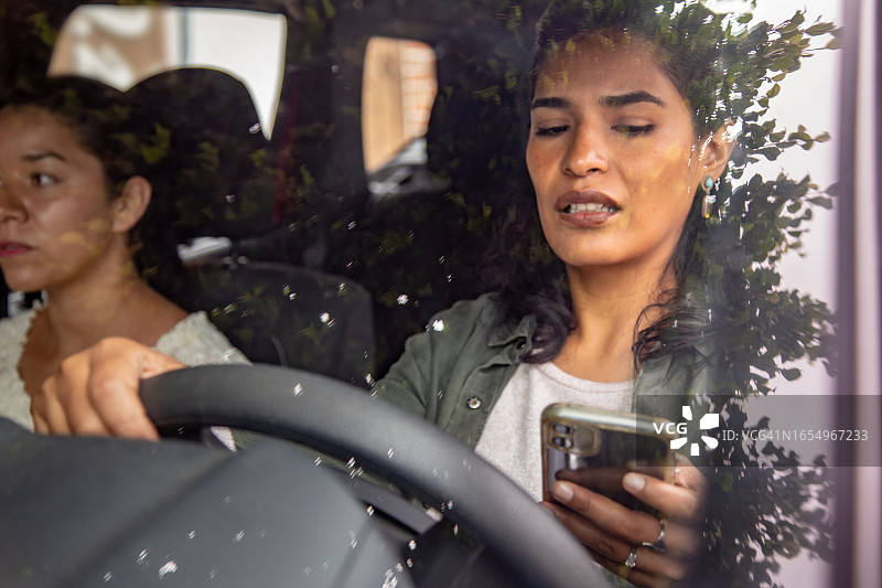 分心司机的概念，一个女人一边开车一边看智能手机图片素材
