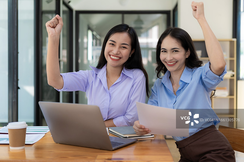 两位女商人面带微笑表达了她们的喜悦。事业成功后，在办公室工作，举起双手表示喜悦。图片素材