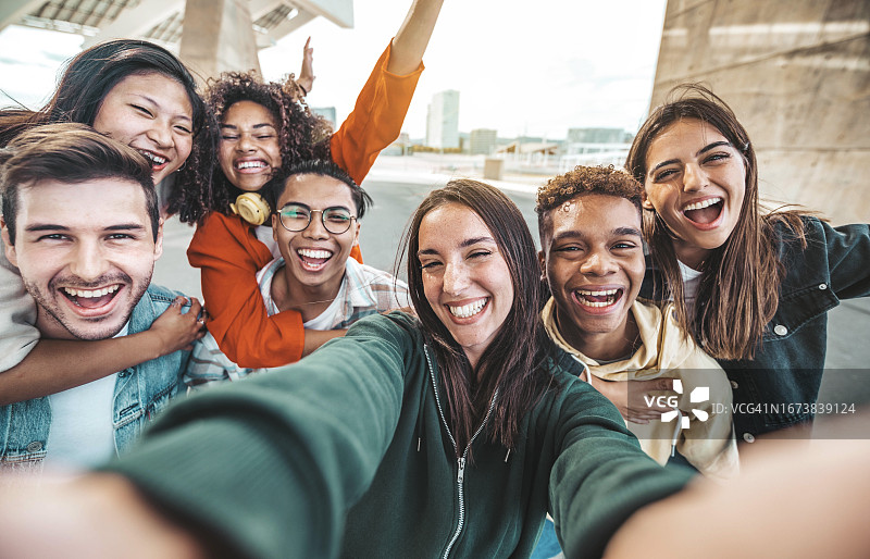 多种族的年轻人一起对着相机笑，一群快乐的朋友用智能手机自拍，年轻人和女孩在户外拥抱的社区概念图片素材