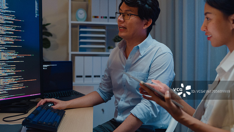 一群亚洲人，软件开发人员，晚上坐在办公室里有多个屏幕的办公桌前，用电脑写代码。程序员开发。图片素材