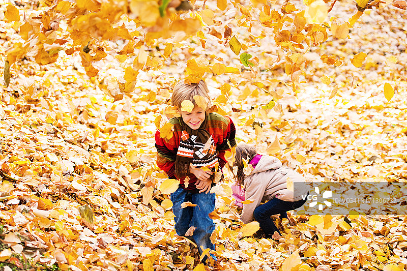 美丽的孩子们在树叶堆里玩耍。图片素材