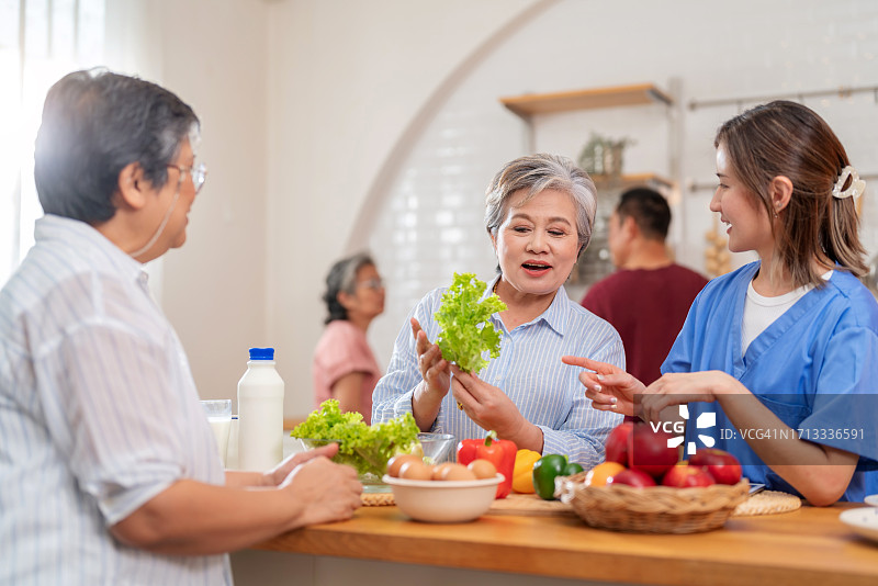 老年人在照顾者的支持下接受营养选择。一位老妇人站在吧台前，正在准备一份新鲜而充满活力的沙拉。护士解释了蔬菜对健康的诸多好处，培养了一种幸福感。图片素材