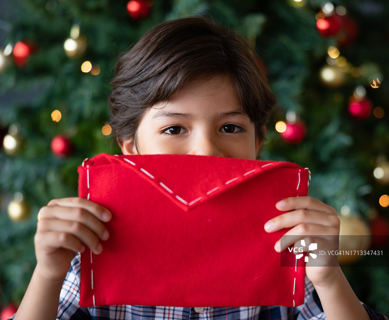 快乐的男孩在圣诞树上给圣诞老人留下一封信图片素材