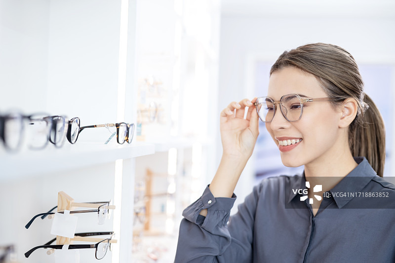 通过试用产品，让消费者做出购买产品的决定，从而增加你的销售额。一位女顾客在眼镜店试穿新眼镜并对着镜子的侧视图。图片素材