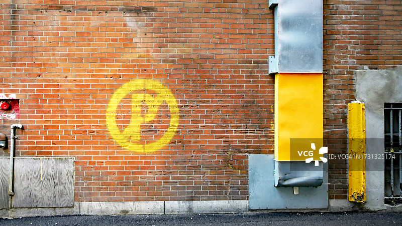 在加拿大魁北克省的蒙特利尔，棕色砖墙上涂着黄色的禁止停车标志，长方形的铝和黄色管道和沥青街道图片素材