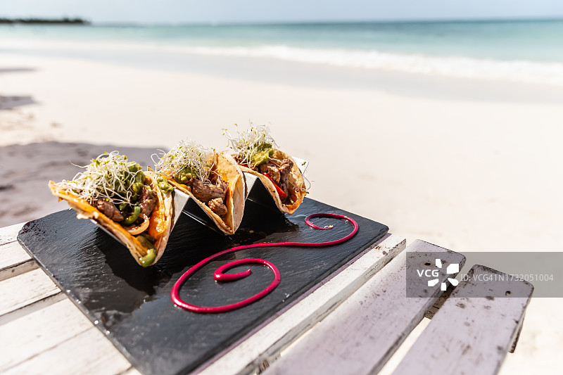 在一个美丽的夏日，三个正宗美味的墨西哥卷饼与烤猪肉和鳄梨酱一起躺在海滩上。图片素材