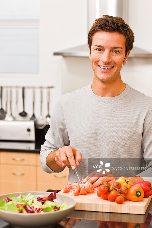 一个微笑的年轻人在厨房切蔬菜的肖像图片素材
