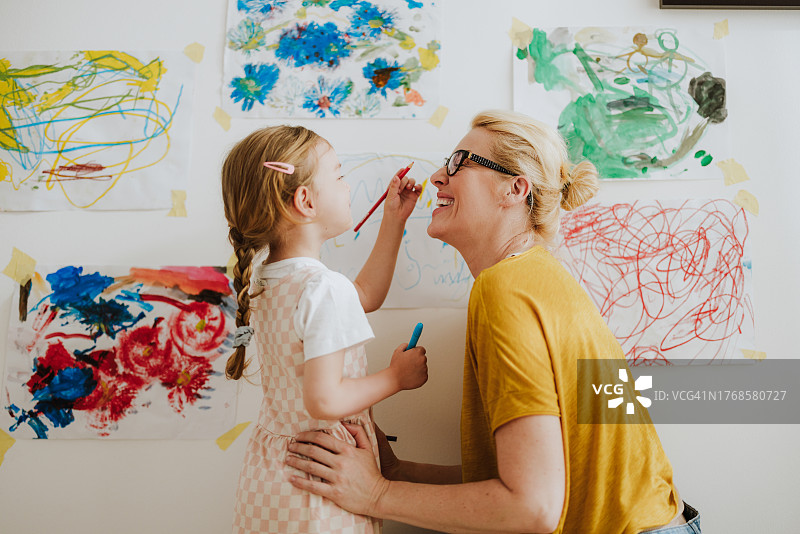一位微笑的母亲和她的小女孩在托儿所的墙上用马克笔画画，玩得很开心图片素材