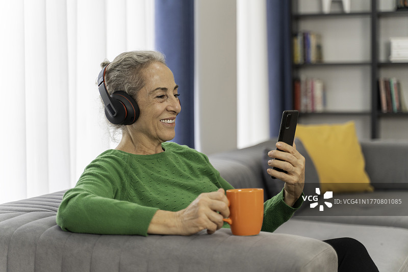 老年妇女戴着耳机在家使用智能手机图片素材