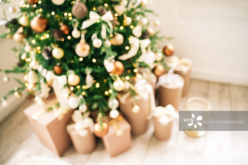 这是一个模糊和散焦的背景，在美丽的装饰杉树下，用蝴蝶结包裹的节日工艺礼物，被蜡烛和圣诞灯照亮图片素材
