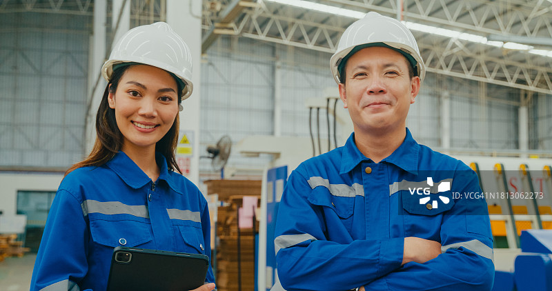 在制造工厂里，专业的亚洲男性和女性工业工程师微笑着看着相机。在制造厂或生产厂工作。图片素材