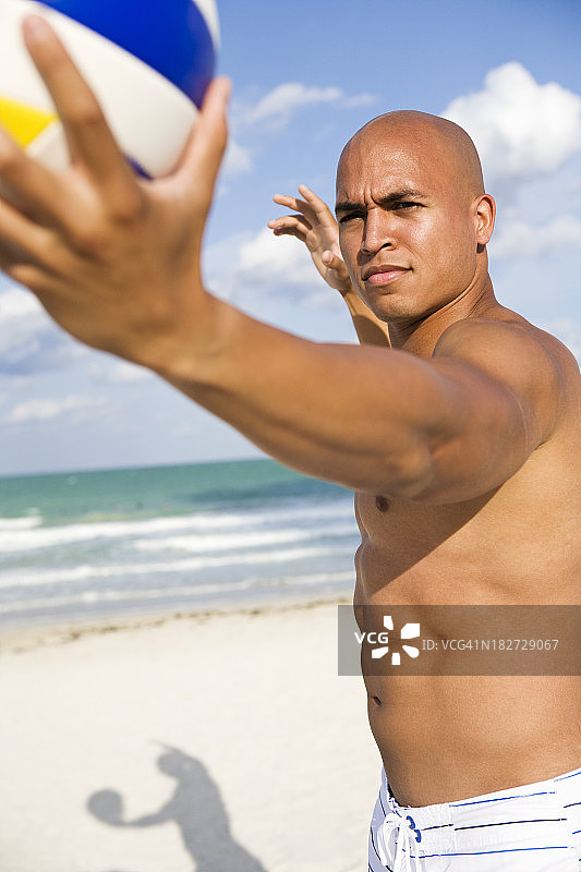 年轻的多民族男子在沙滩上发球排球图片素材