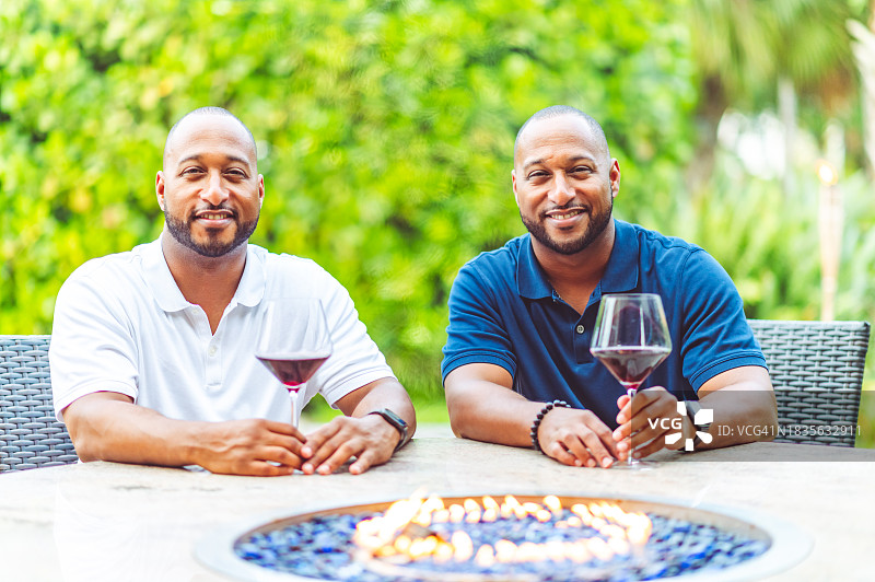 英俊的非裔美国成年双胞胎兄弟在户外露台上一起享受一杯葡萄酒图片素材