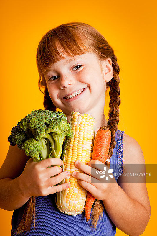 快乐，微笑的年轻女孩抱着西兰花，玉米，胡萝卜图片素材