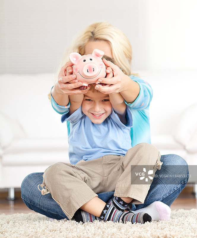 小男孩和他的妈妈把钱放进小猪存钱罐里图片素材