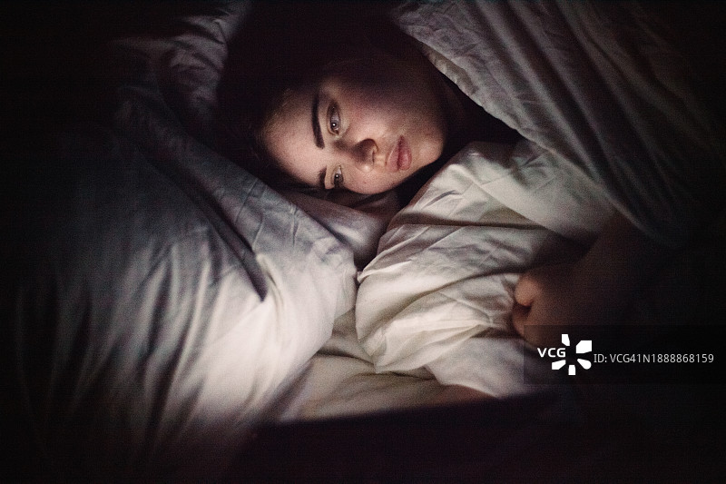 年轻女子晚上躺在床上玩数码平板电脑图片素材