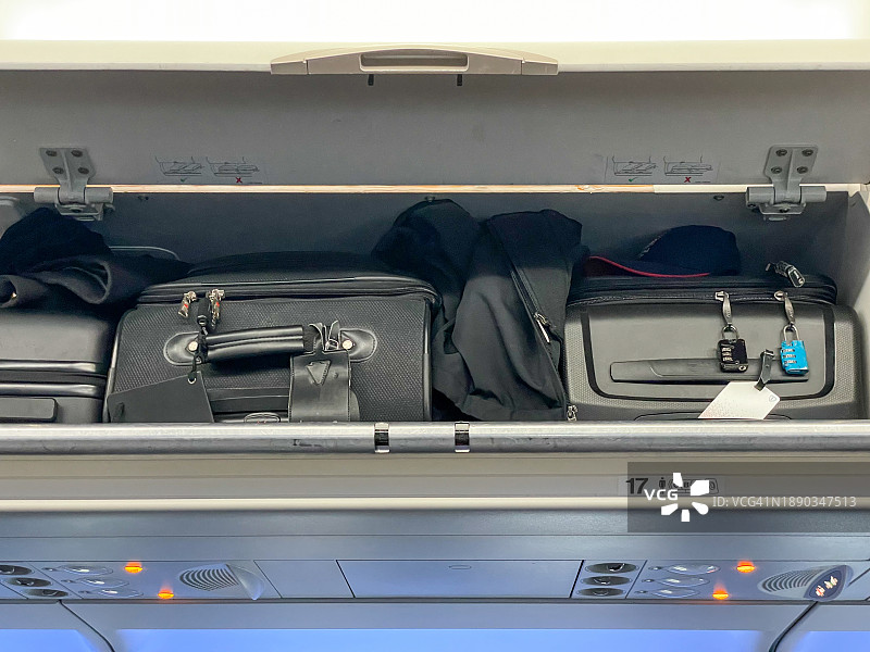 起飞前登机——过大的行李和行李被塞进头顶的储物舱，无法正常关闭。通勤者在旅行时打包了很多行李，避免托运行李费用的风险由他们自己承担图片素材