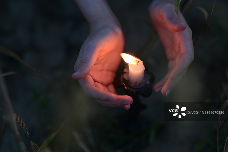 田野里，一个女孩在烛光下温暖她的手掌图片素材