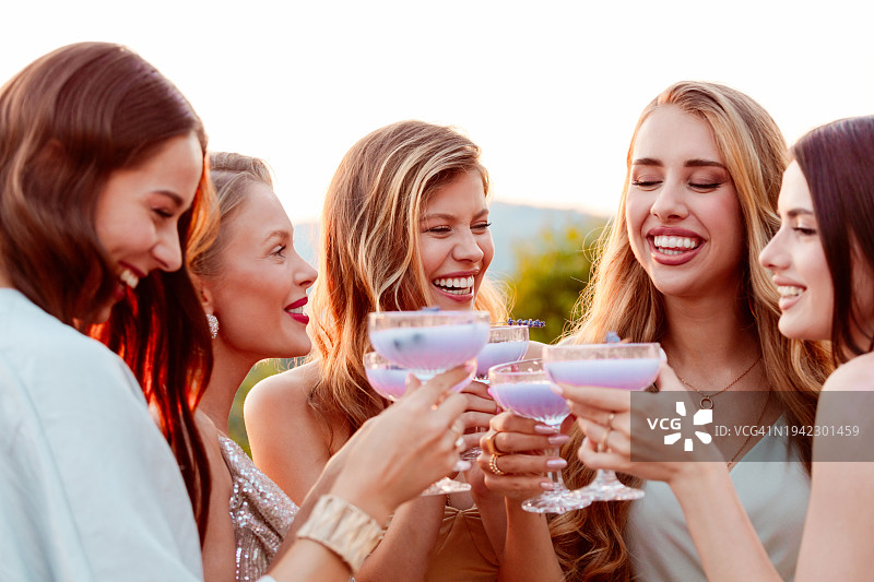 女性朋友们穿着优雅的礼服，在日落时分在户外喝薰衣草饮料图片素材