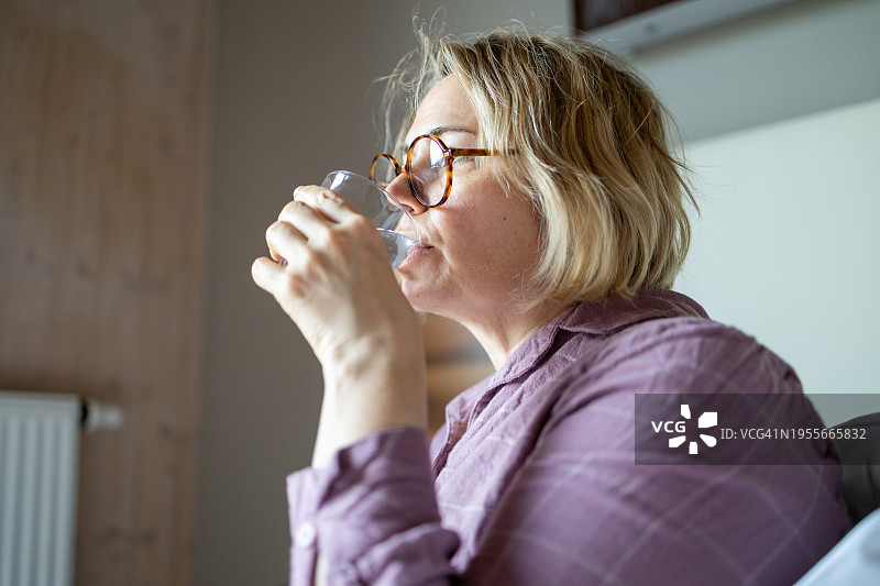 成熟的女人在家里用玻璃杯喝水图片素材