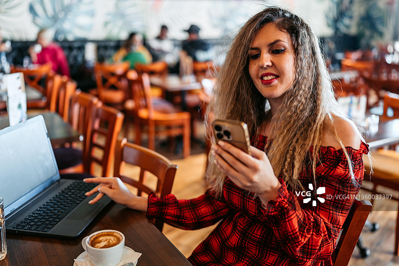 年轻女子一边用笔记本电脑工作，一边在咖啡店喝咖啡图片素材