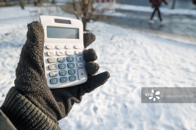 人们用计算器计算成本。背景是一条下雪的街道，人们沿着街道行走。图片素材