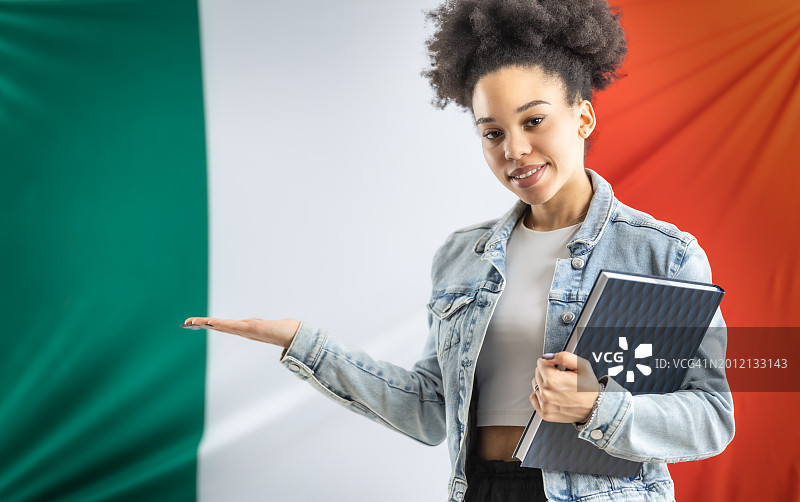非裔美国女学生站在意大利国旗前，拿着书包和笔记本电脑，为产品或信息提供位置。图片素材