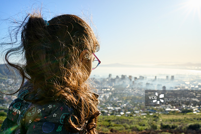 小女孩站在山顶的瞭望台上看风景优美的城市图片素材