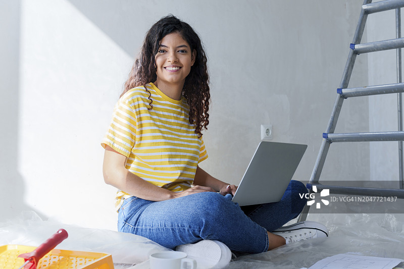 微笑的女人坐在新家的笔记本电脑前图片素材