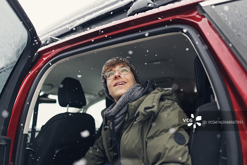 一个十几岁的男孩坐在车里，在冬天的公路旅行中享受雪图片素材