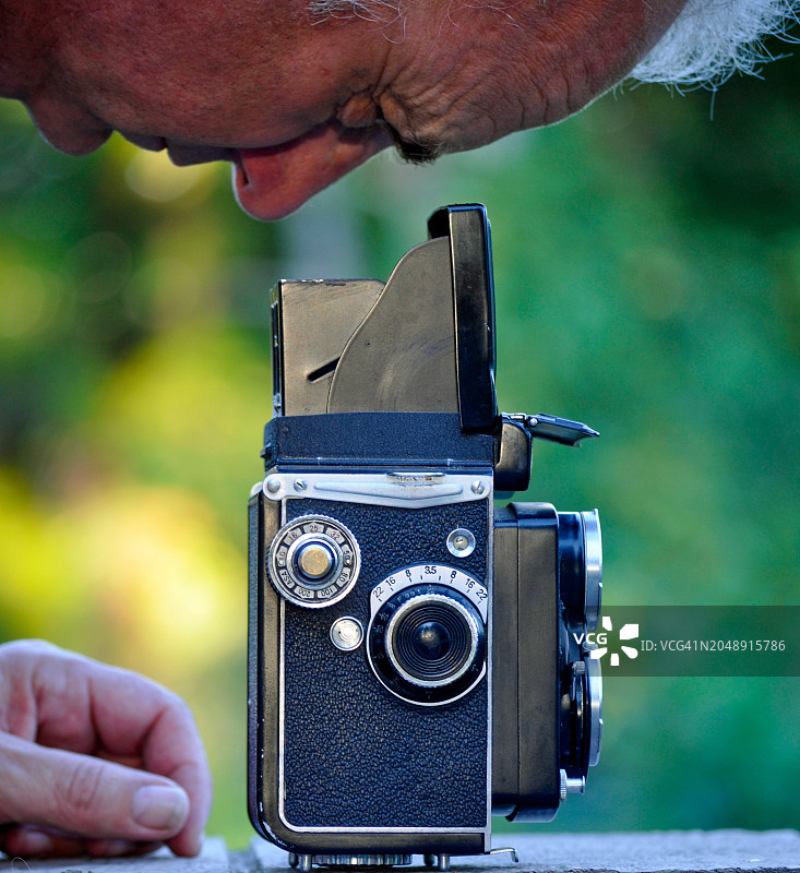 一个男人的特写，他正在看向一台老式中画幅相机的取景器图片素材