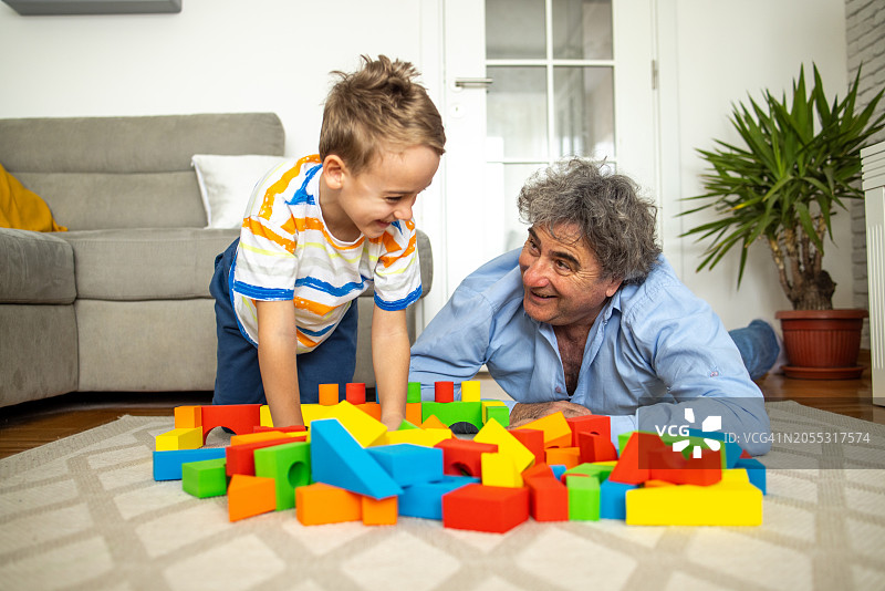 爷爷和孙子在客厅的地板上玩玩具。图片素材