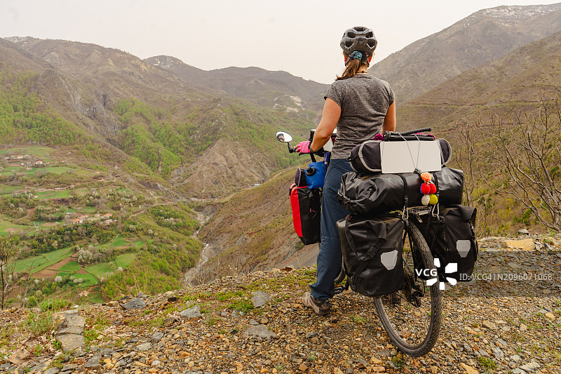 一个中年骑自行车的人停下来欣赏崎岖的山地景观，在阴天下拍摄了一张完整的照片图片素材