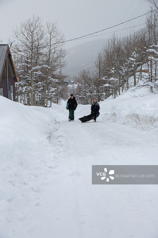 两个男孩在落基山脉被雪覆盖的街道上滑行。图片素材