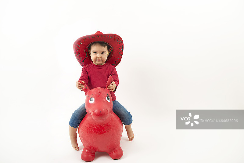 戴着红色牛仔帽的小女孩骑着玩具马图片素材