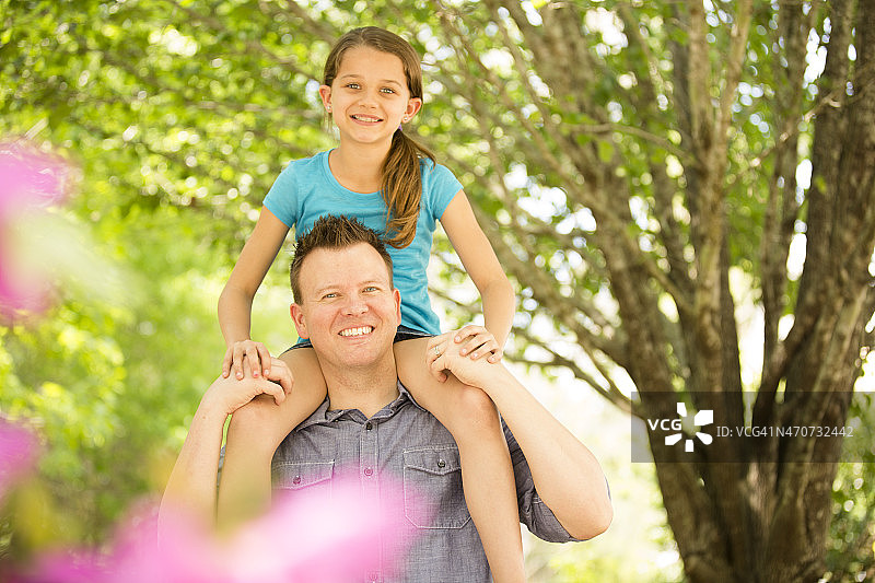 父亲把女儿扛在肩上。公园或院子里。夏天的乐趣。图片素材