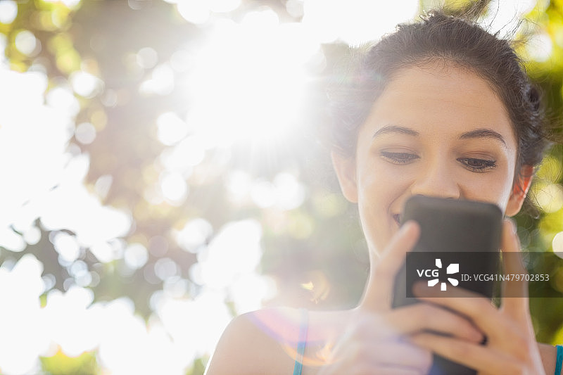 快乐的黑发女人用她的智能手机发短信图片素材