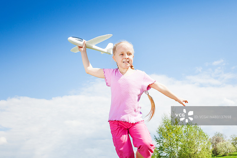 快乐微笑的女孩在跑步中拿着飞机玩具图片素材