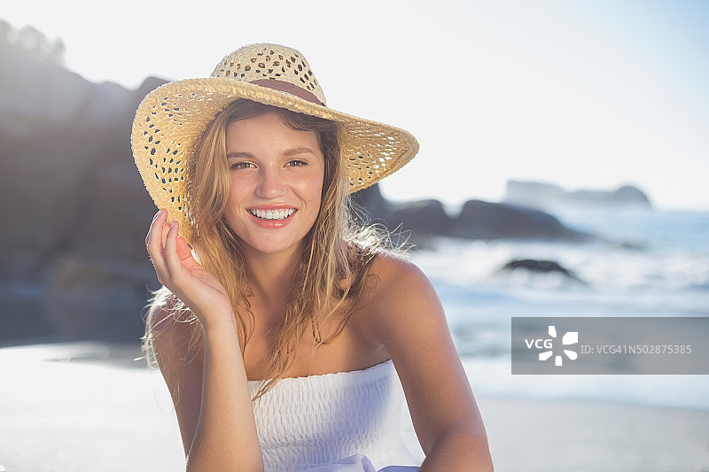 穿着太阳裙坐在沙滩上微笑的金发美女图片素材