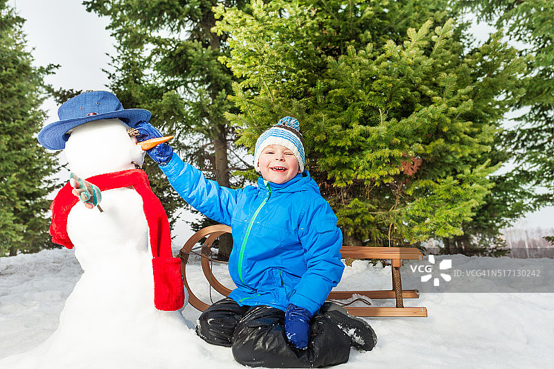 小男孩用雪橇在公园堆雪人图片素材