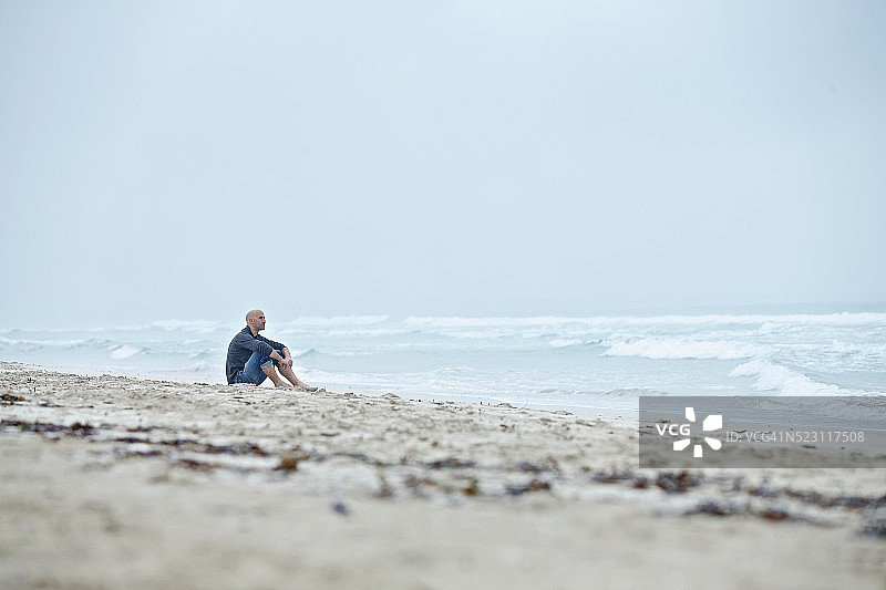 西班牙巴利阿里群岛，马略卡岛，一个年轻人坐在海边的沙滩上图片素材