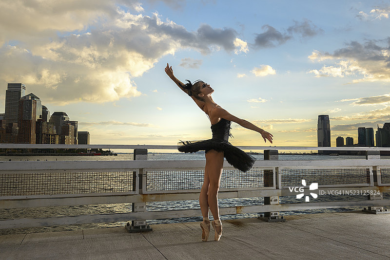 美国纽约，一名芭蕾舞女演员穿着黑色芭蕾舞裙，在夕阳下翩翩起舞图片素材